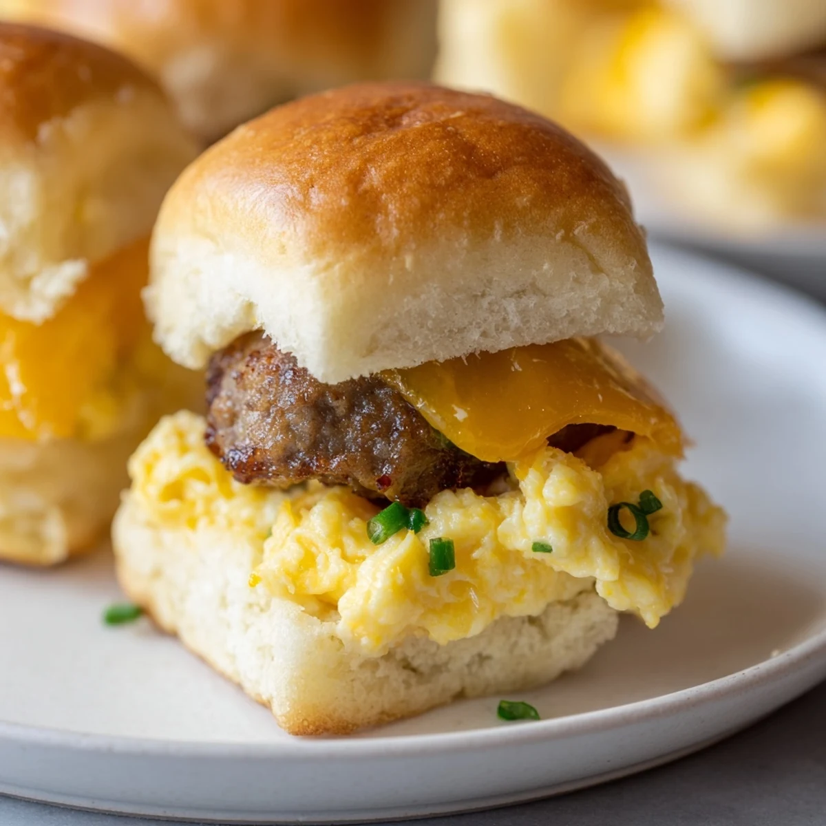 Perfectly assembled mini breakfast sliders featuring fluffy eggs, a sausage patty, and melted cheddar cheese are served.