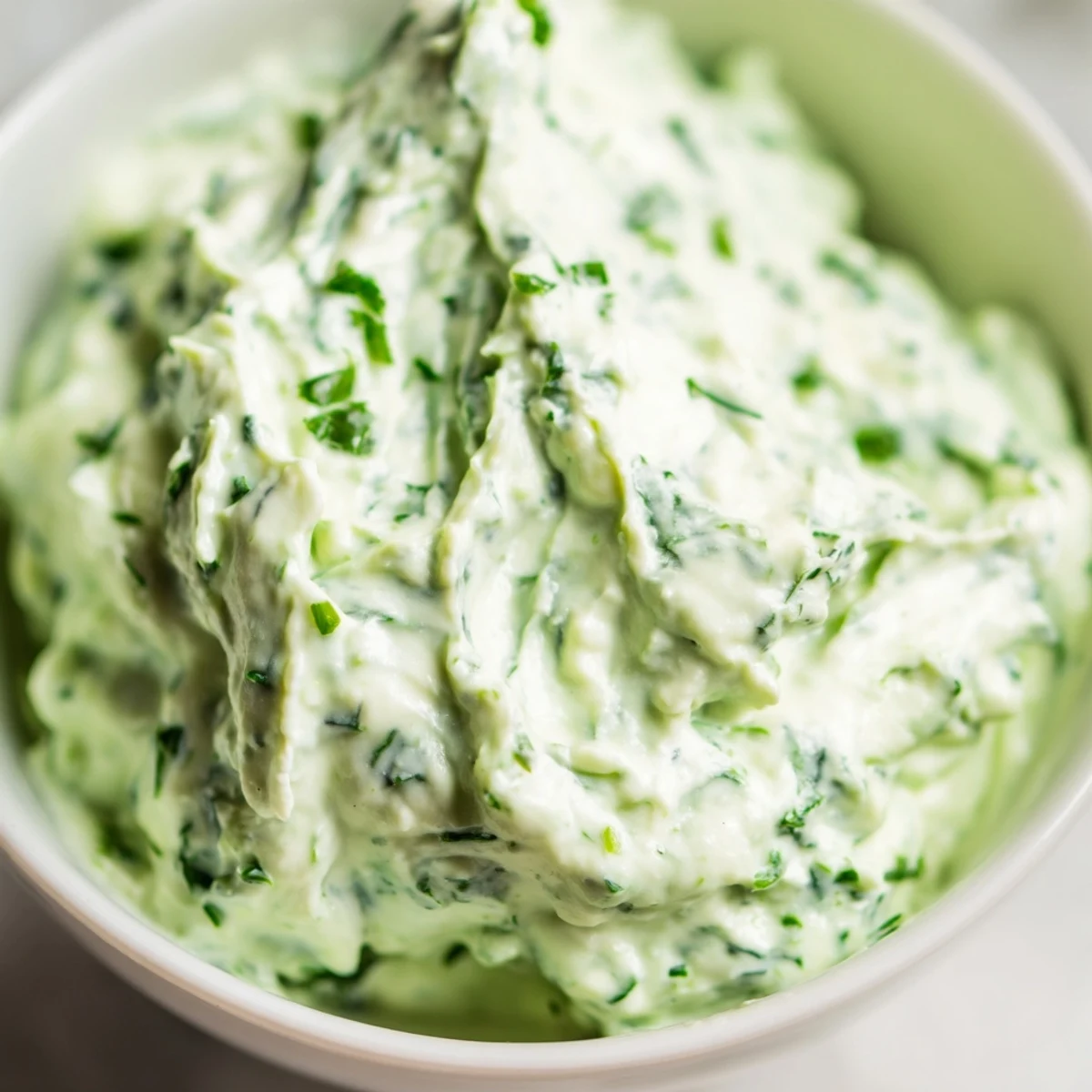 A close-up view of the vibrant green dip, garnished with fresh chives and parsley, ready for scooping with crunchy carrot and cucumber slices.
