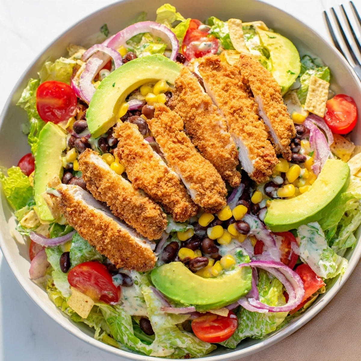 Close-up view of golden, spiced chicken tenders garnishing a Tex-Mex salad with avocado and cheddar cheese.