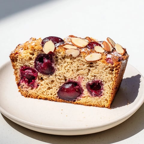 A slice of Cherry Almond Loaf Cake, showing juicy cherries and a golden, crumbly top.