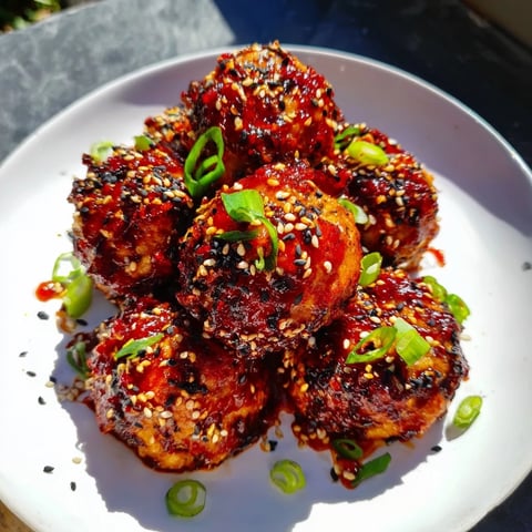 Golden-brown Spicy Honey-Glazed Chicken Meatballs glistening in a sweet and spicy sauce await serving.