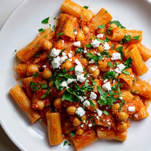 Steaming bowl of spicy Harissa Chickpea Pasta, bright red sauce with parsley garnish, ready to eat.