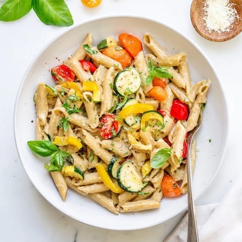 Creamy One-Pot Pasta Primavera with zucchini, bell peppers, and cherry tomatoes, garnished with fresh basil.  