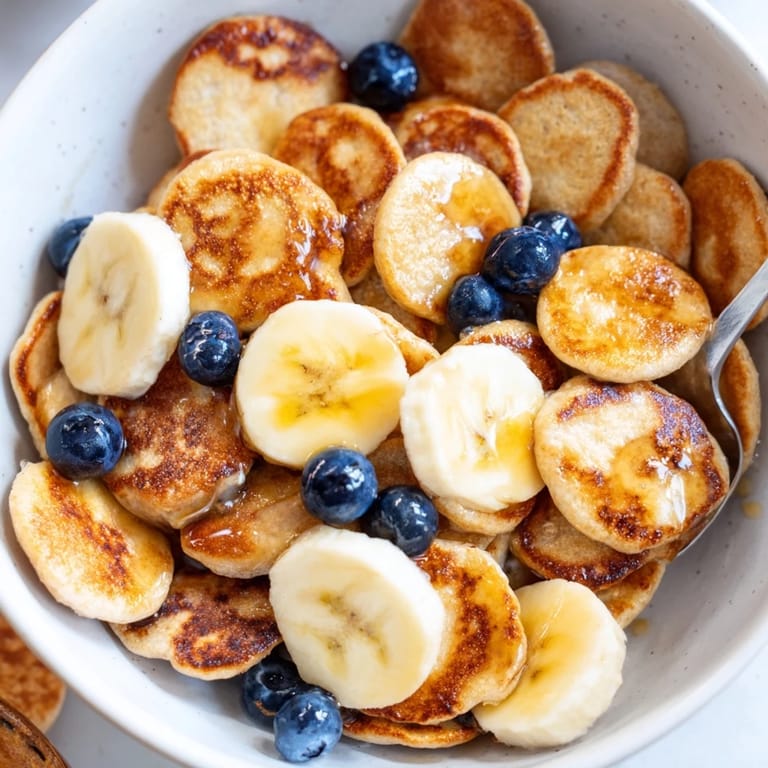 Crispy mini pancake cereal served in a bowl with milk and banana slices. 