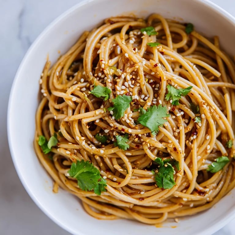 Overhead view of a vibrant Spicy Sesame Noodle Salad tossed with fresh cilantro, spring onions, and chopped peanuts, ideal for a quick vegetarian lunch.