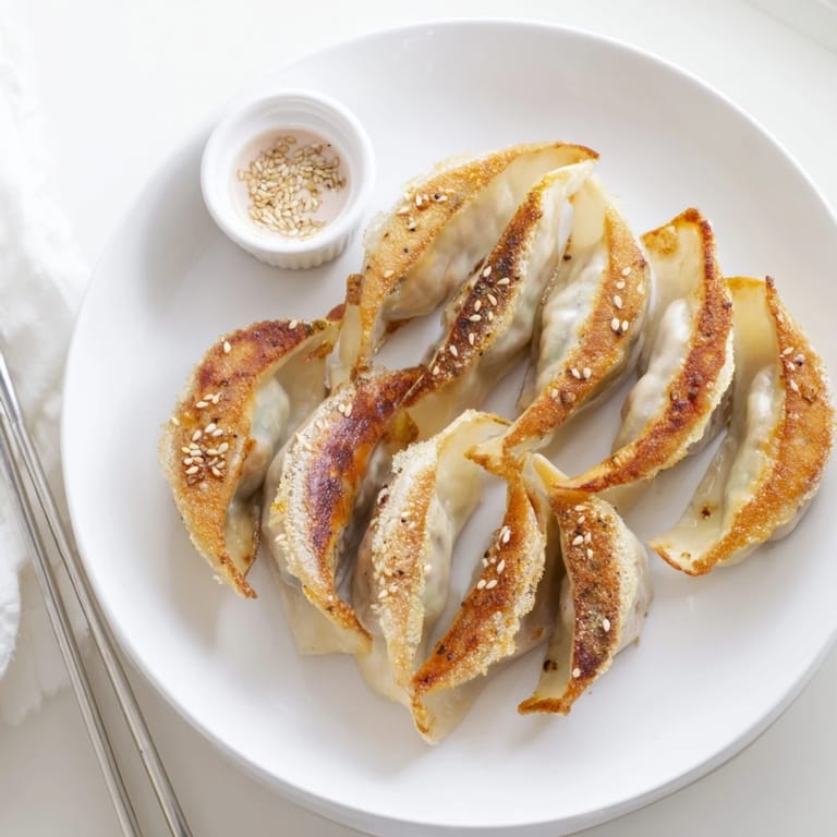 A close-up of crispy-edged smashed gyozas, revealing a savory pork and cabbage filling served with a tangy soy-vinegar dip.